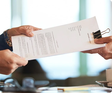 Close-up of two people exchanging a prepared bid document with binder clip, illustrating bid prep and submission services