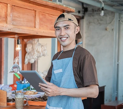 Vendor coordinating orders using a tablet at an outdoor market stand with supplies in the background